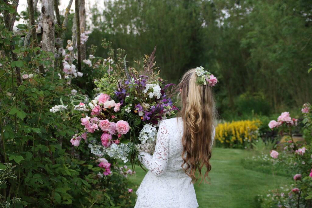 A woman carries a huge bunch of freshly cut garden roses, hydrangeas, scented white deutzia through an abundant summer garden. Photo: Heather and Hedgerow.