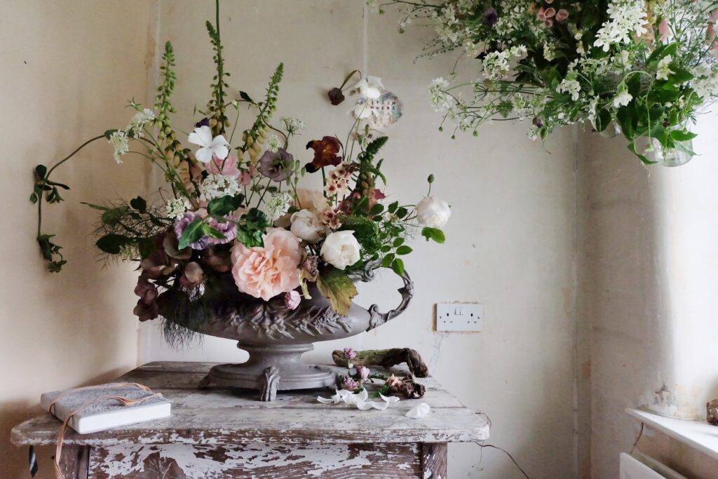 A beautifully etched dark metal urn filled with foxgloves, corncockles, scented roses and creme brulee fox by Firenza in celebration of British Flowers Week.