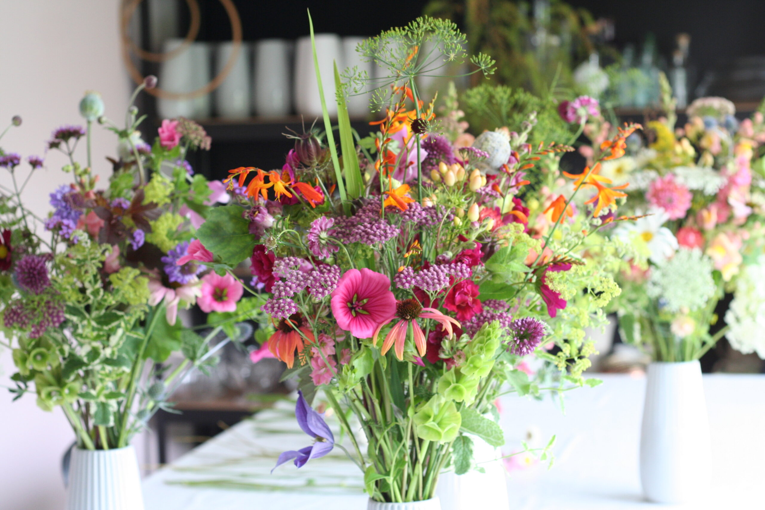 Colourful summer jugs of British cut flowers by Henthorn Farm Flowers. Pink male, orange crocosmia and vivid green bells of Ireland.