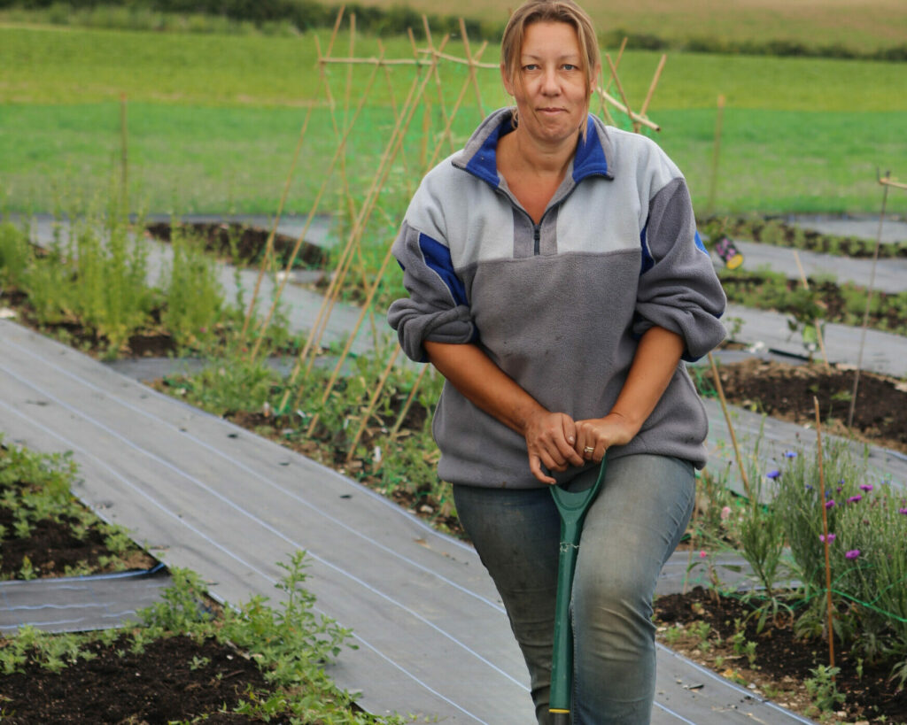 Debbie of Nature's Posy stands with her digging fork on her cut flower farm, preparing the soil for her seedlings.