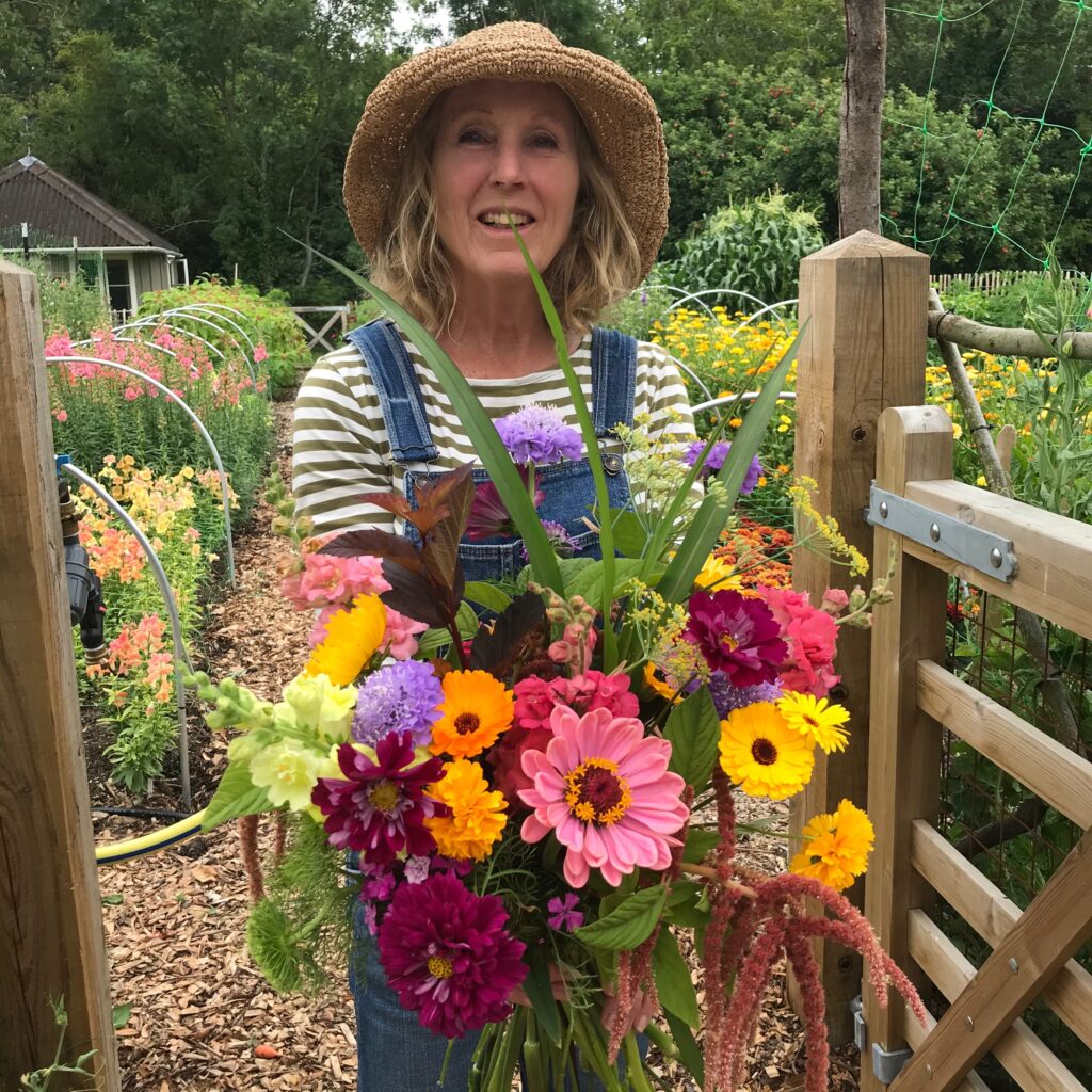 The airy flowers of fennel add floaty height to this bright bouquet by Eileen of Tinshead Flowers. She holds it in her hands standing in the gateway to her flower field.