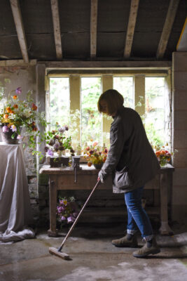 Sarah of Simply By Arrangement sweeps up after arranging flowers in her Yorkshire window for British Flowers week 2021