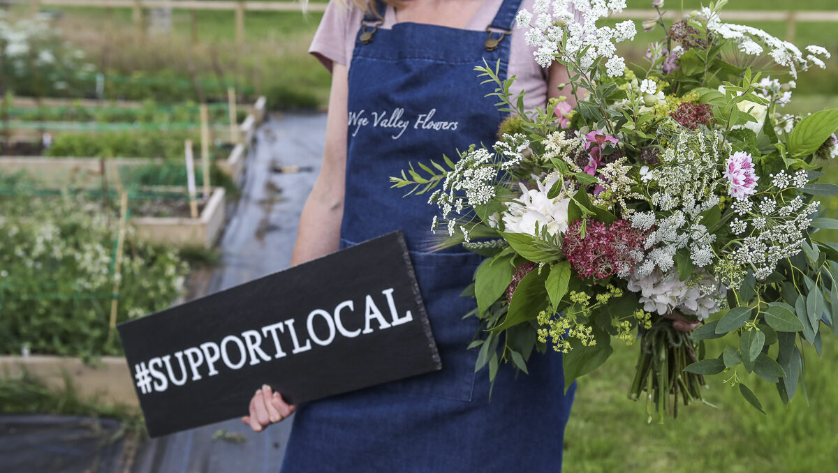 Lucy of Wye Valley Flowers holds a sign showing their support for local business