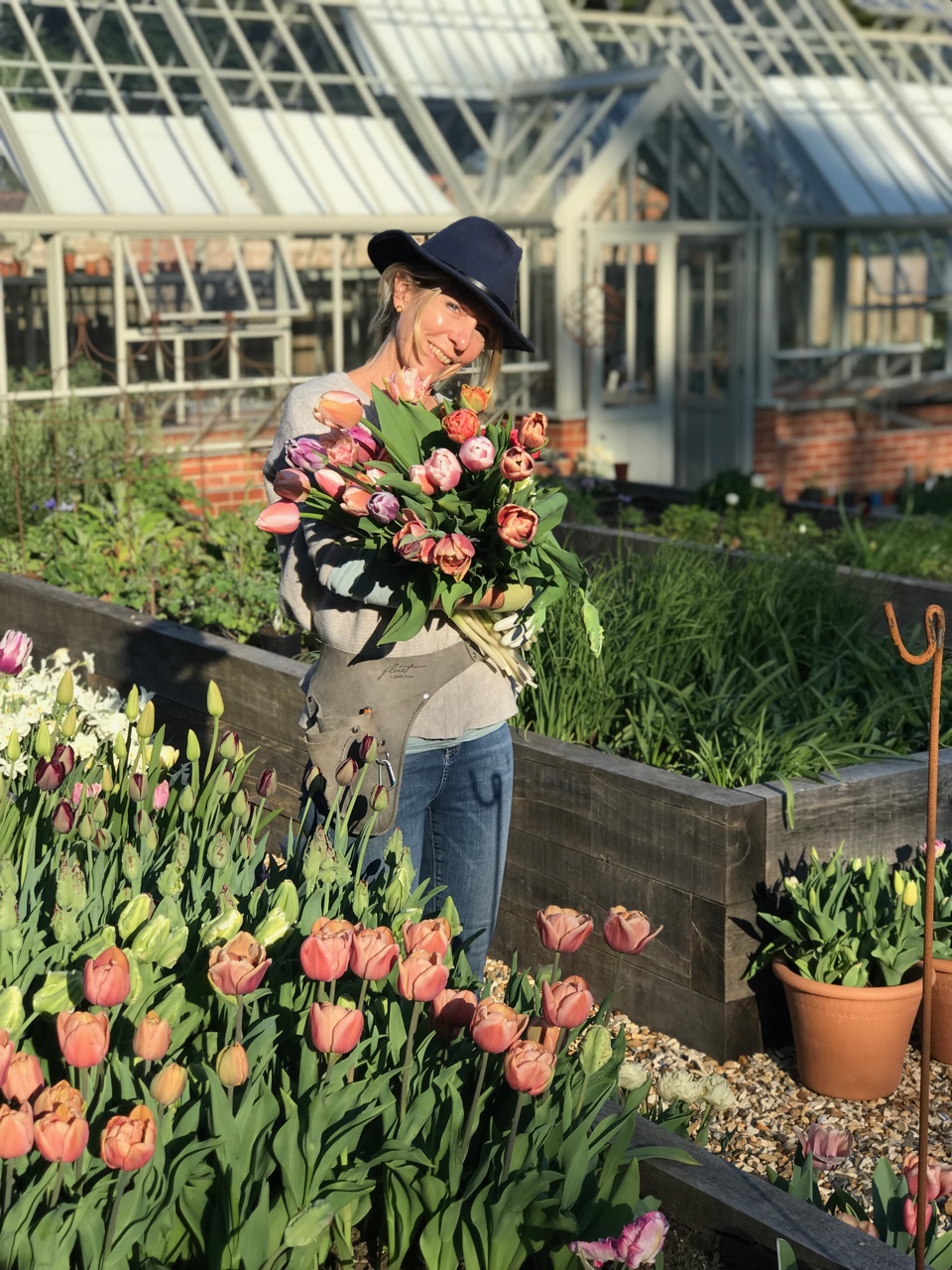 Jill Houston of Little Park Flowers with armfuls of tulips next to raised beds and her traditional greenhouse