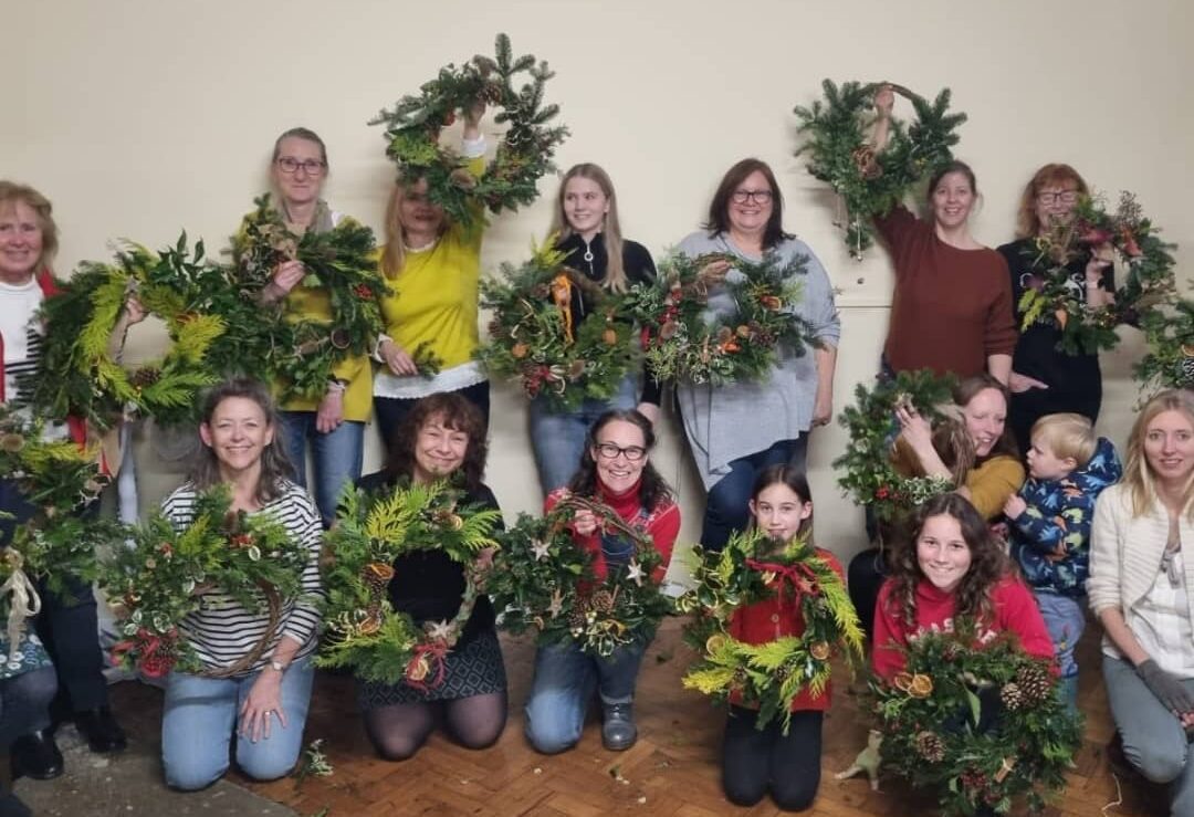 A happy crowd of attendees at a wreath workshop run by Wildeblooms & Willow showing off their all natural, all British grown creations