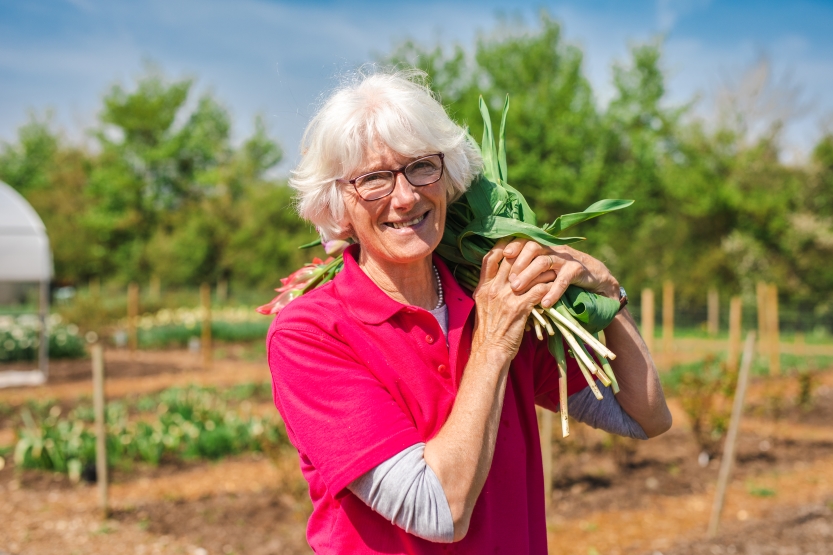 Gill Hodgson, founder of Flowers from the Farm, holds a bunch of British grown cut flowers and smiles wearing her FFTF signature pink polo shirt.